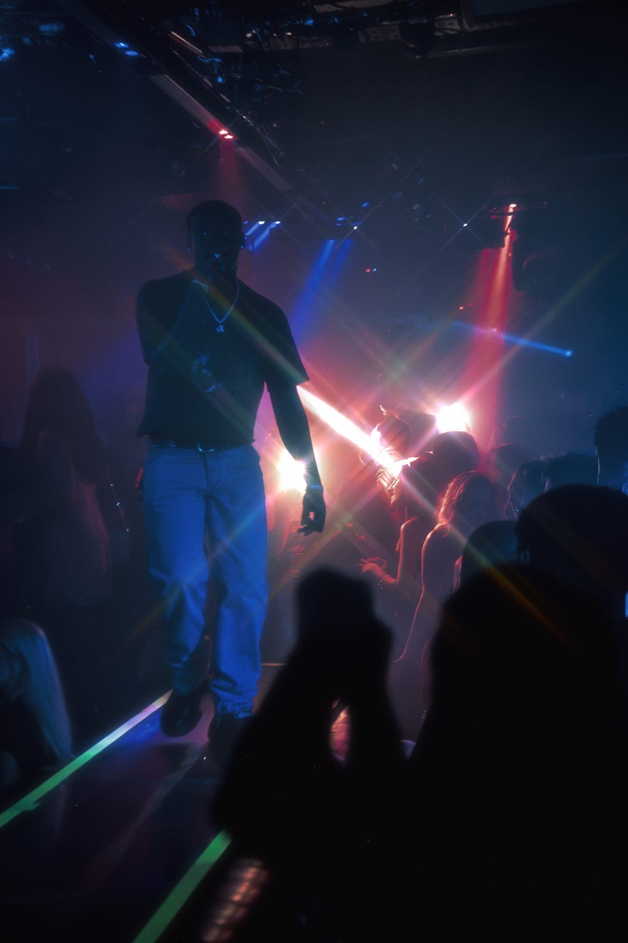Silhouetted performer on a raised stage above a crowd under red and blue club lights