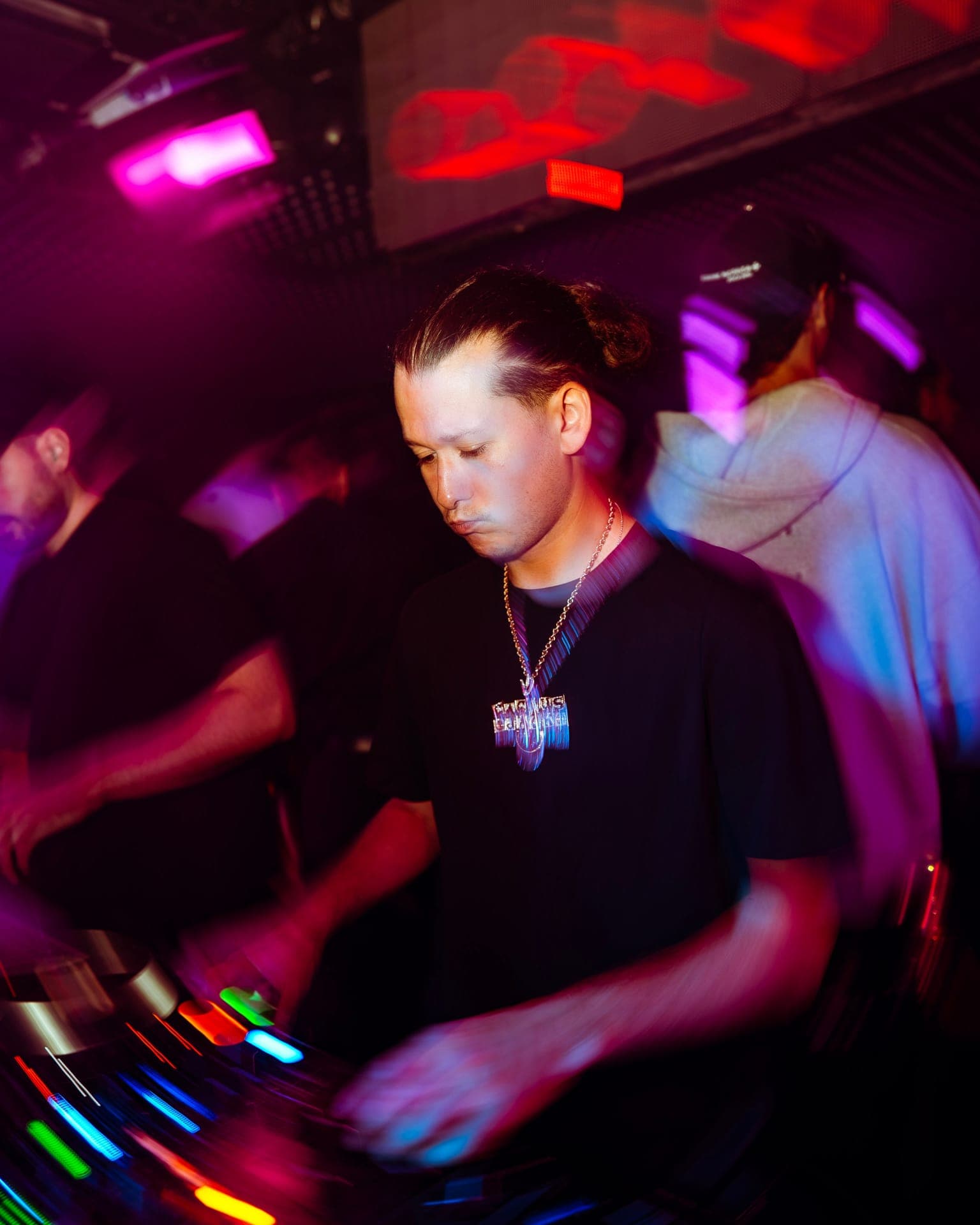 A DJ mixing on illuminated decks under pink and red club lighting