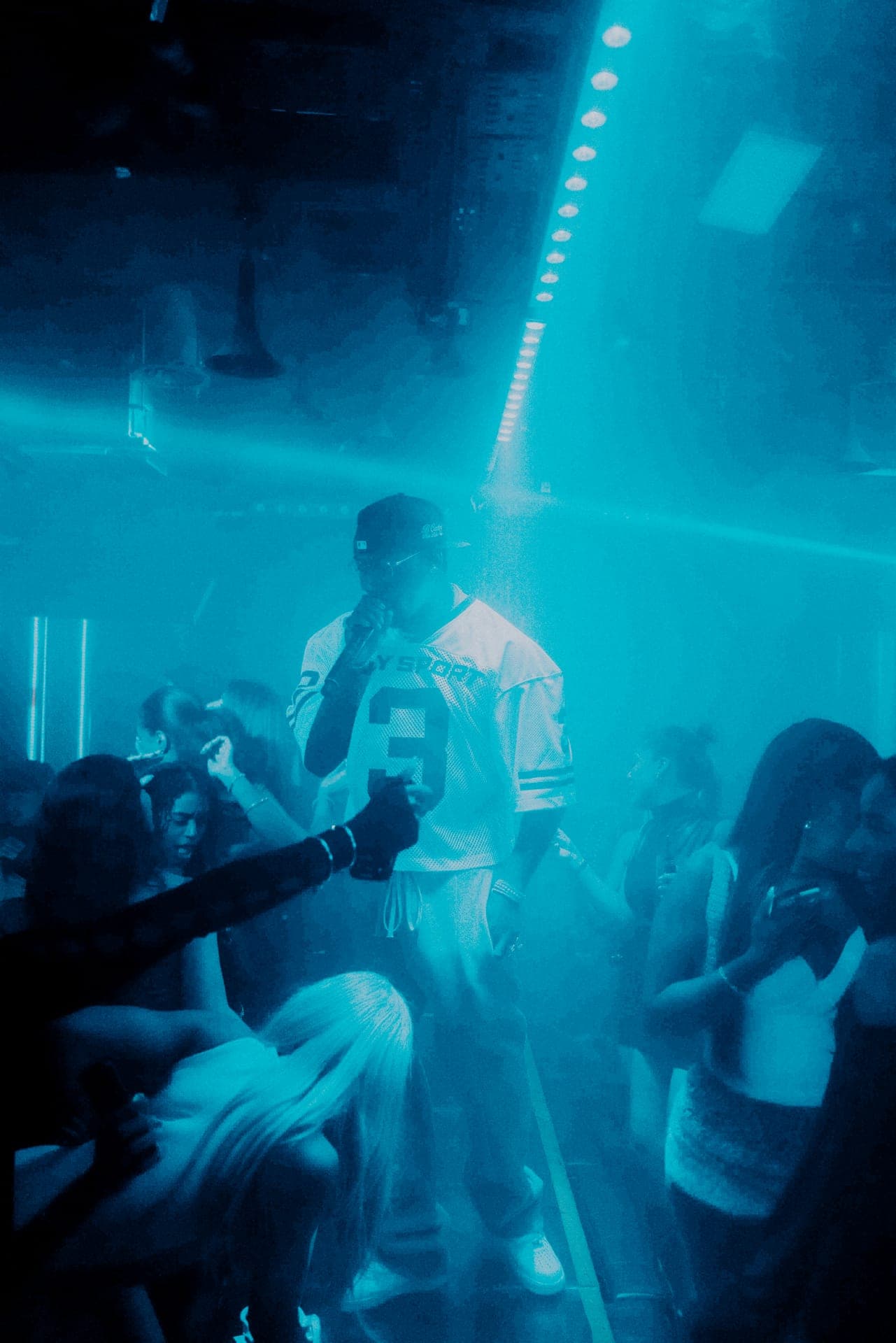 A performer with a microphone in a crowded nightclub lit in blue